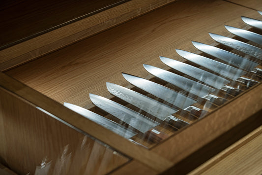Several Japanese kitchen knives from Hitohira displayed side-by-side in a wooden drawer.